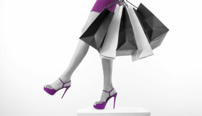 Giovane donna indossa gonna e scarpe con tacco di colore viola. In mano tiene diverse borse, ha appena fatto shopping