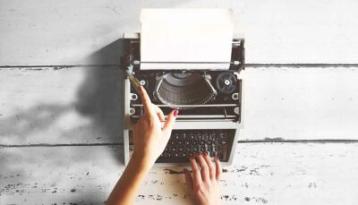 immagine in bianco e nero. Due mani di donna inquadrate dall'alto che stanno digitando i tasti di una vecchia macchina da scrivere