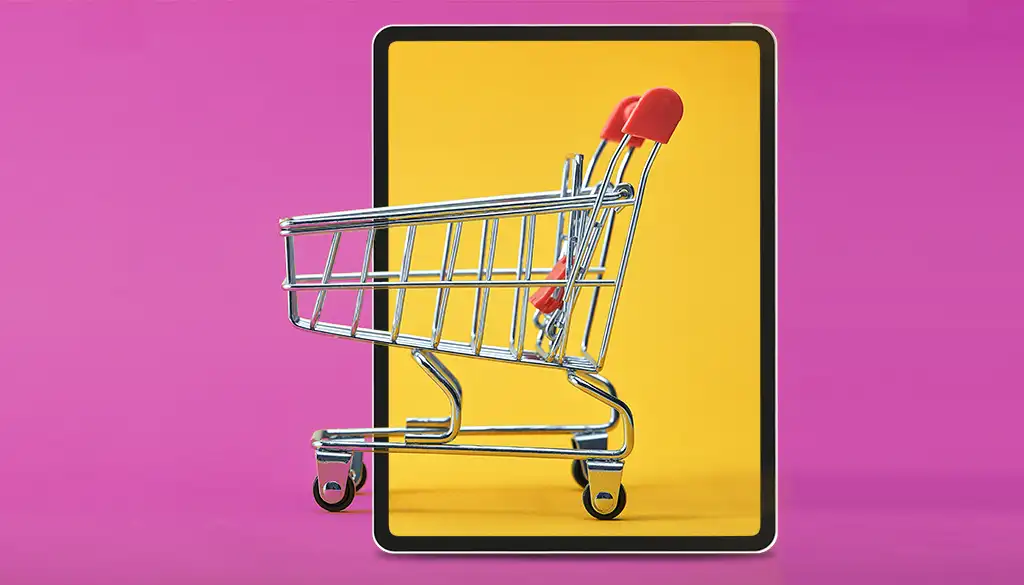 un carrello della spesa in metallo posizionato su un display di un tablet con fondo giallo. Lo sfondo dell'immagine e di colore viola.