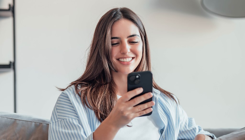 una ragazza sorridente sta guardando con attenzione uno smartphone