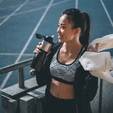 ragazza fa sport in un campo sportivo mentre beve da una borraccia