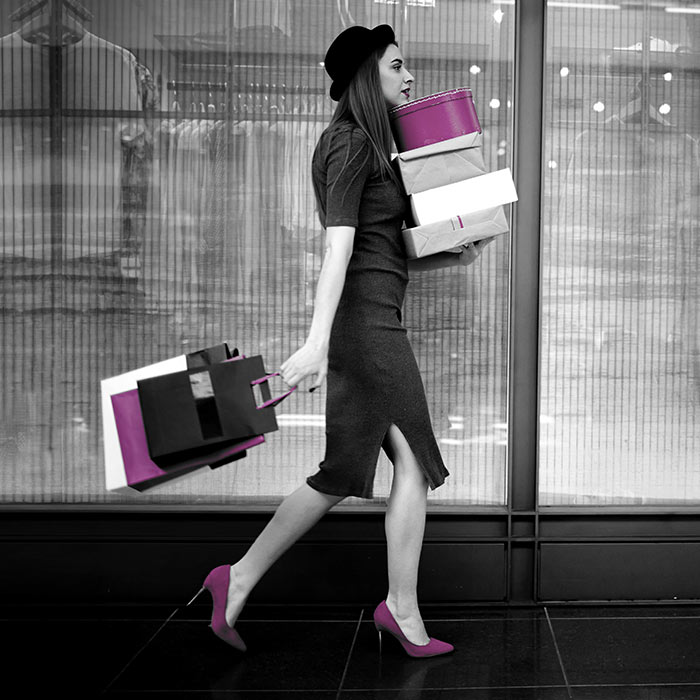 fotografia bianco e nero con alcuni elementi viola. Una donna elegante cammina per strada con diversi pacchi in mano. Ha appena fatto shopping